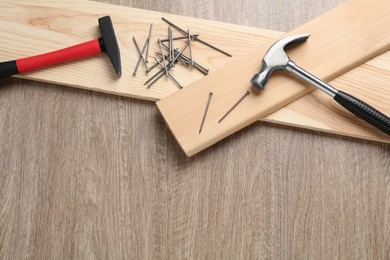 Photo of Hammers, metal nails and planks on wooden table, flat lay. Space for text