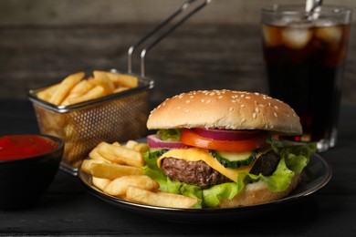 Photo of Delicious burger, soda drink and french fries served on black table