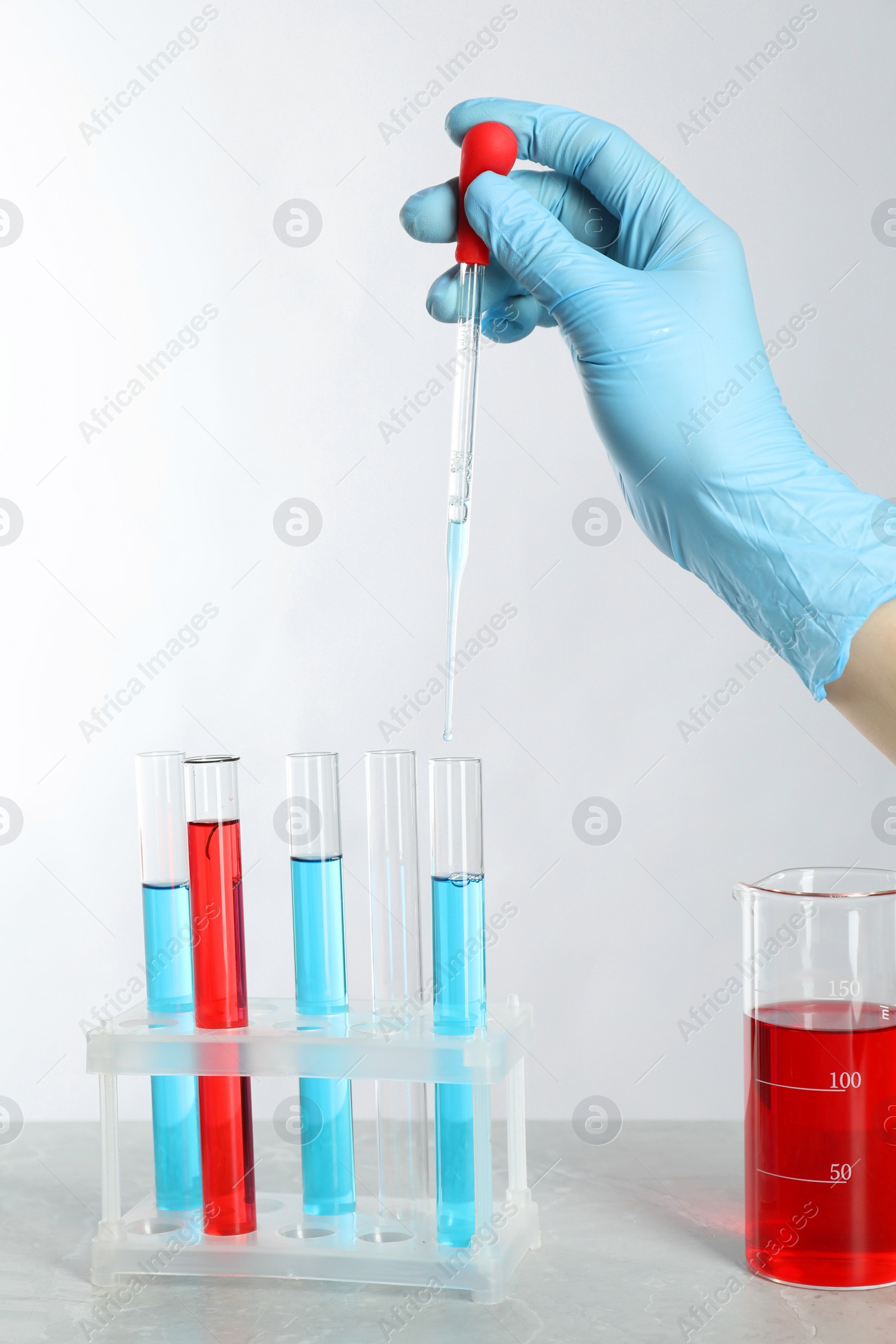 Photo of Scientist dripping liquid from pipette into test tube at grey marble table, closeup