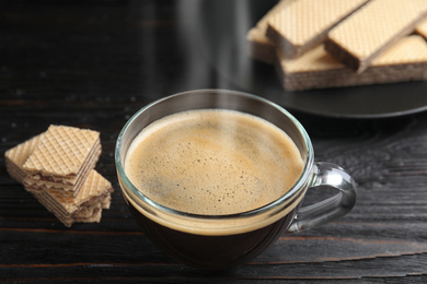 Photo of Delicious coffee and wafers on black wooden table