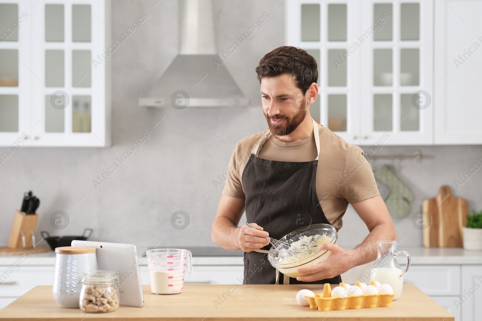 Photo of Man making dough while watching online cooking course via tablet in kitchen