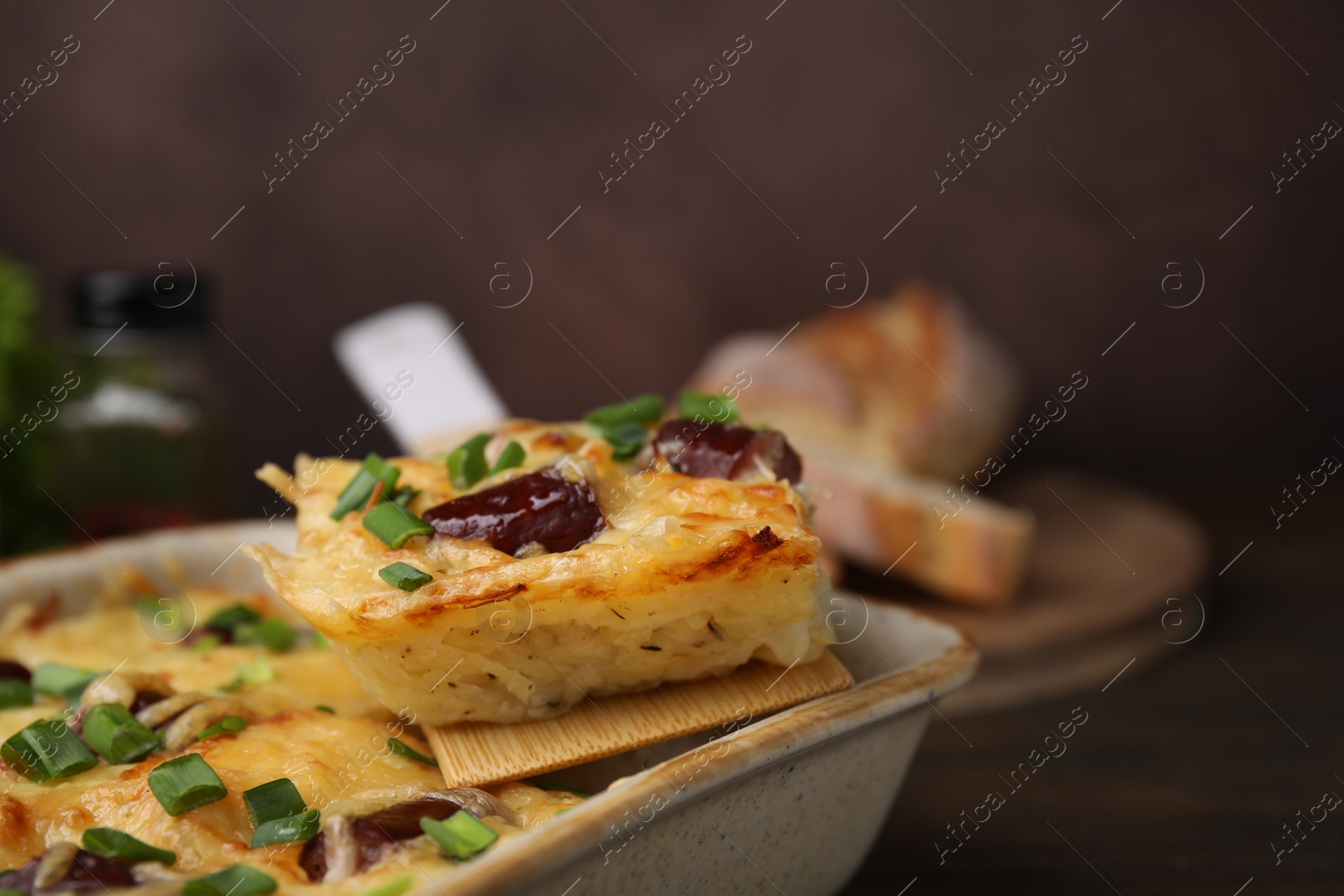 Photo of Taking piece of tasty sausage casserole from baking dish at table, closeup. Space for text