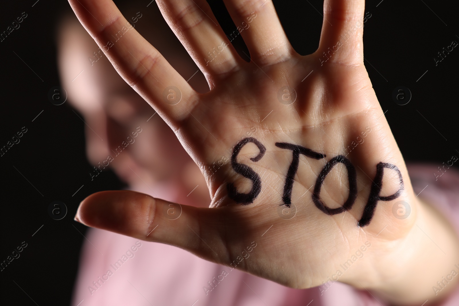 Photo of Woman with word Stop written on hand against dark background, closeup. Domestic violence concept