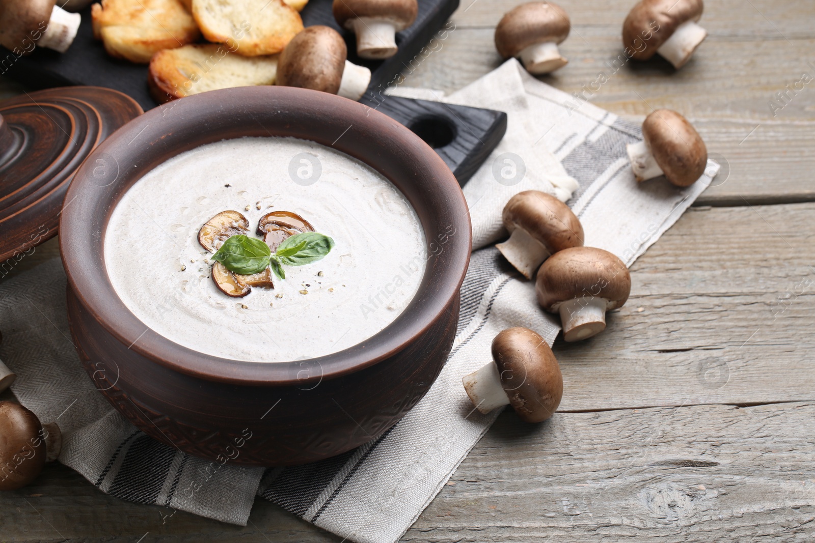 Photo of Delicious homemade mushroom soup in ceramic pot and fresh ingredients on wooden table. Space for text