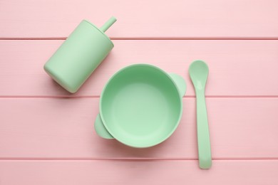 Set of plastic dishware on pink wooden background, flat lay. Serving baby food