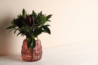 Vase with beautiful bouquet on white wooden table near beige wall. Space for text