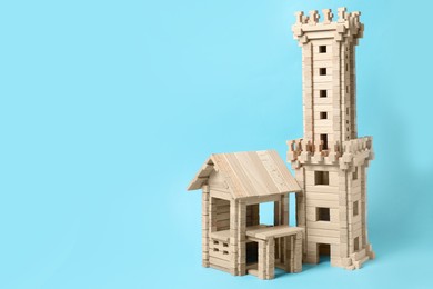 Photo of Wooden tower and house on light blue background, space for text. Children's toy