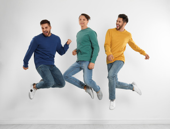 Group of young men in stylish jeans jumping near white wall