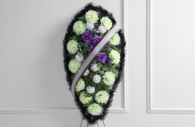 Funeral wreath of plastic flowers with ribbon near white wall