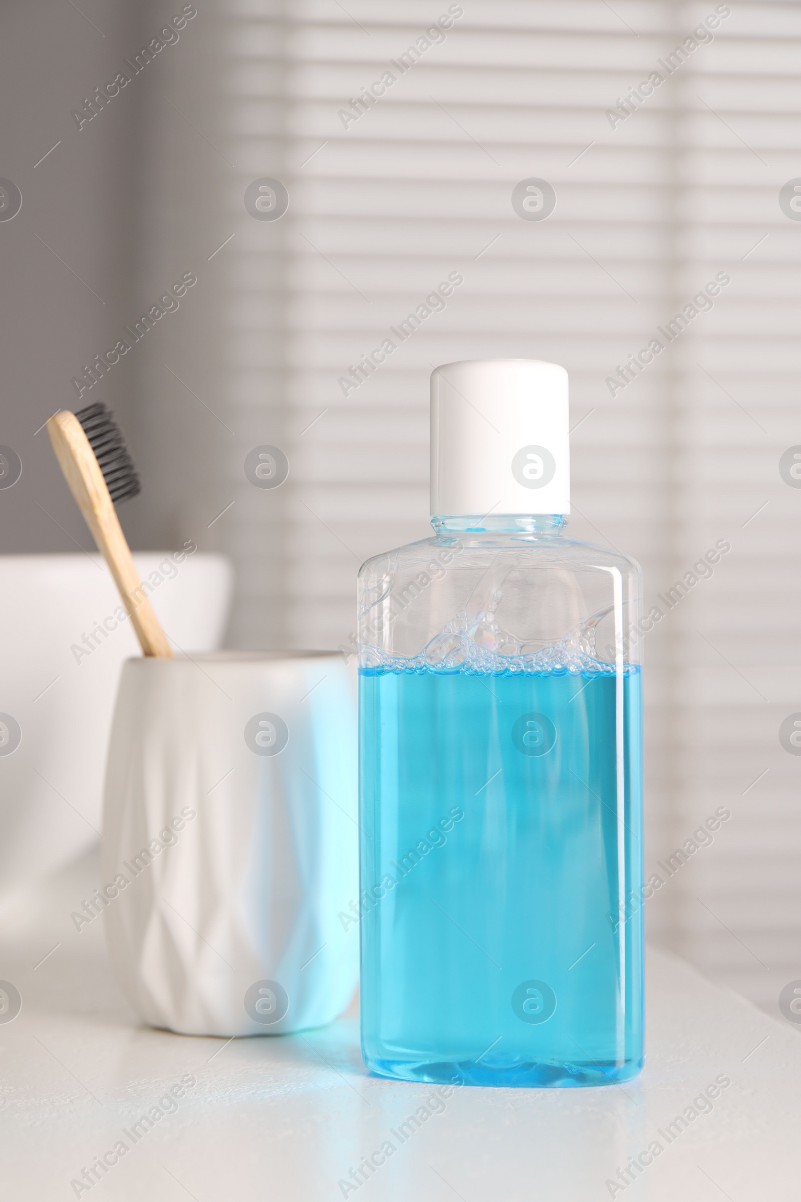 Photo of Bottle of mouthwash and toothbrush on white table in bathroom