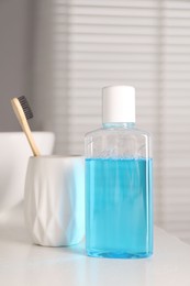 Photo of Bottle of mouthwash and toothbrush on white table in bathroom