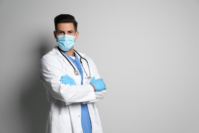 Doctor in protective mask and medical gloves against light grey background. Space for text