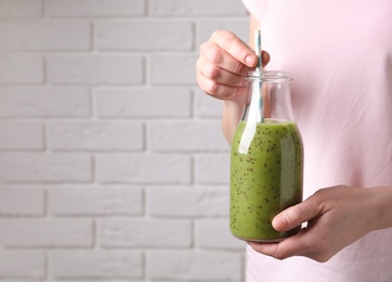 Photo of Woman with delicious kiwi smoothie near white brick wall, closeup. Space for text