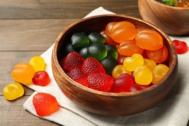 Delicious gummy candies in bowl on wooden table