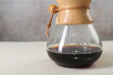 Glass chemex coffeemaker with tasty drip coffee on white table, closeup. Space for text