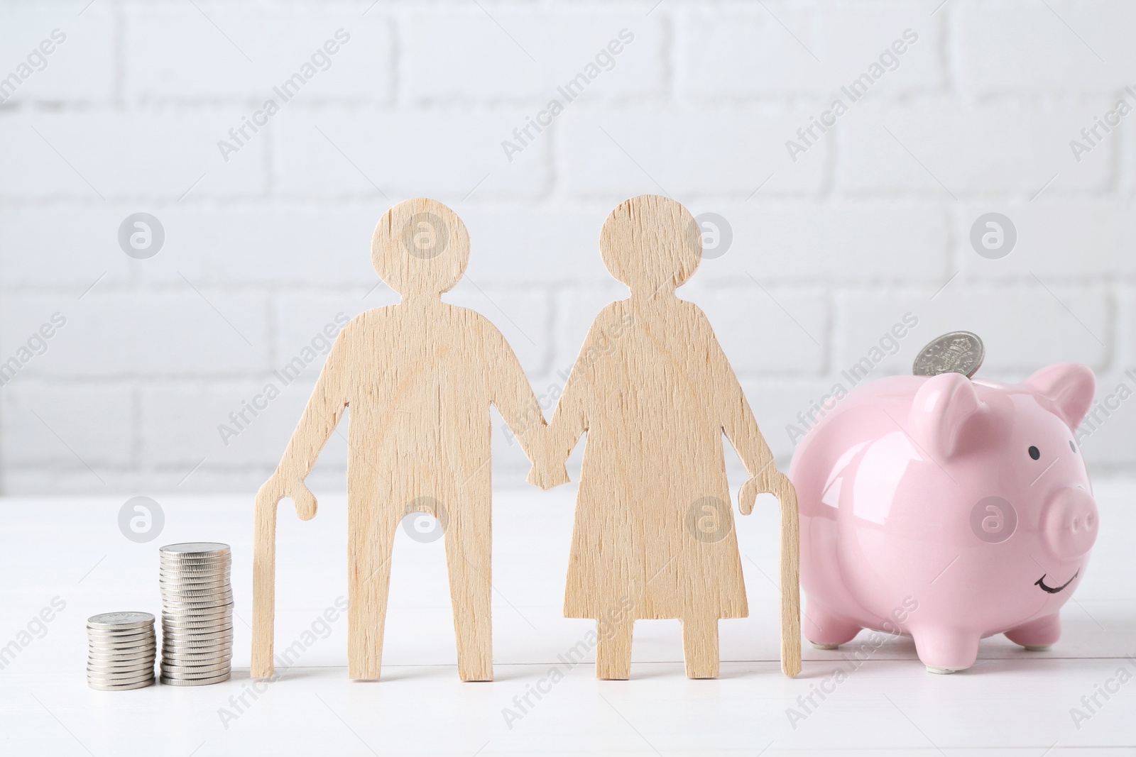 Photo of Pension savings. Figure of senior couple, piggy bank and stacked coins on white table