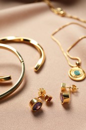 Photo of Elegant earrings, bracelets and necklace on beige cloth, closeup