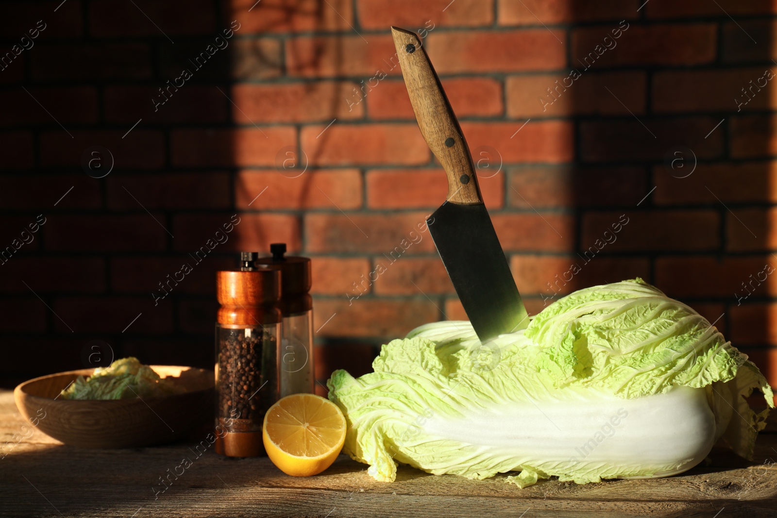 Photo of Fresh Chinese cabbage, knife, spices and lemon on wooden table