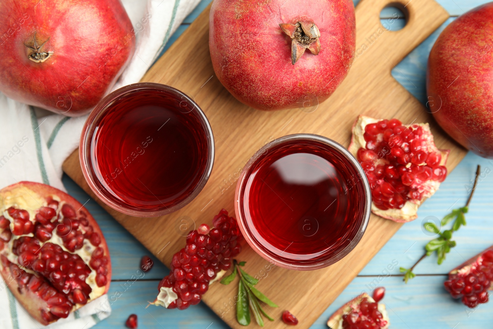 Photo of Glasses of pomegranate juice and fresh fruits on light blue wooden table, flat lay
