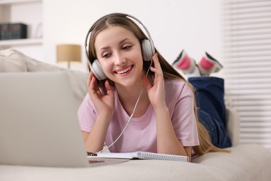 Photo of Online learning. Smiling teenage girl in headphones near laptop on sofa at home