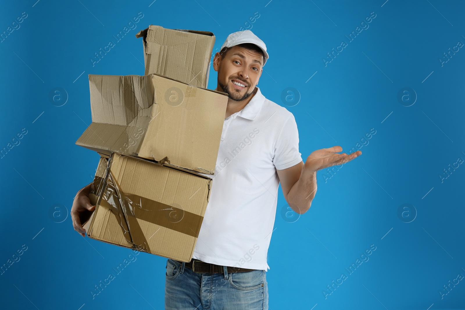 Photo of Emotional courier with damaged cardboard boxes on blue background. Poor quality delivery service