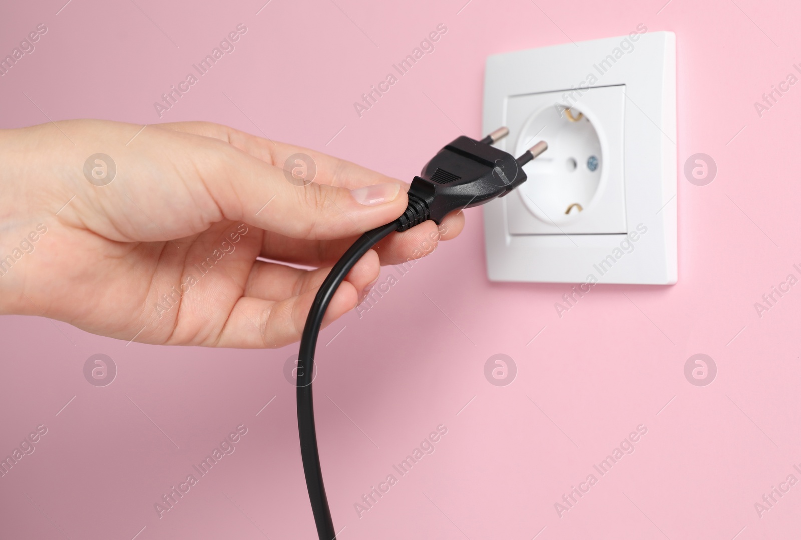 Photo of Woman inserting plug into power socket on pink wall, closeup. Electrical supply