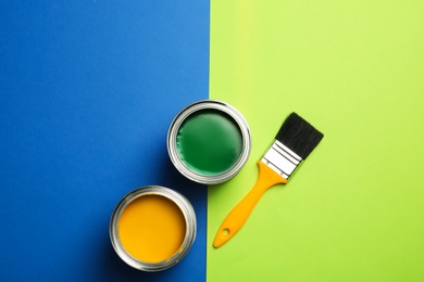 Open paint cans and brush on color background, top view