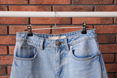 Rack with stylish jeans near brick wall, closeup