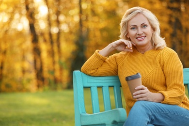 Photo of Beautiful mature woman with cup of coffee on bench in park
