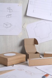 Photo of Creating packaging design. Drawings, boxes and stationery on table, closeup