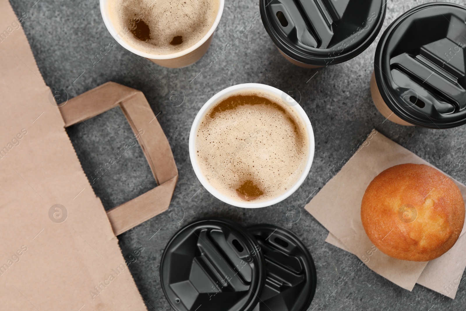 Photo of Coffee to go. Paper cups with tasty drink and muffin on grey table, flat lay