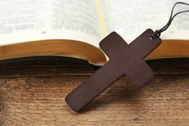 Photo of Christian cross and Bible on wooden table, closeup