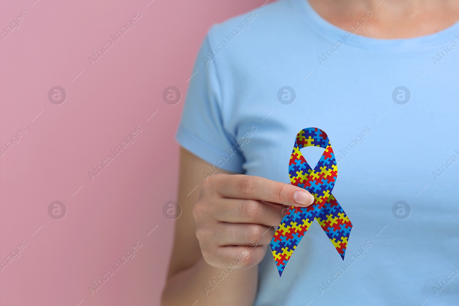 Image of World Autism Awareness Day. Woman with colorful puzzle ribbon on pink background, closeup