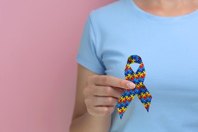 Image of World Autism Awareness Day. Woman with colorful puzzle ribbon on pink background, closeup