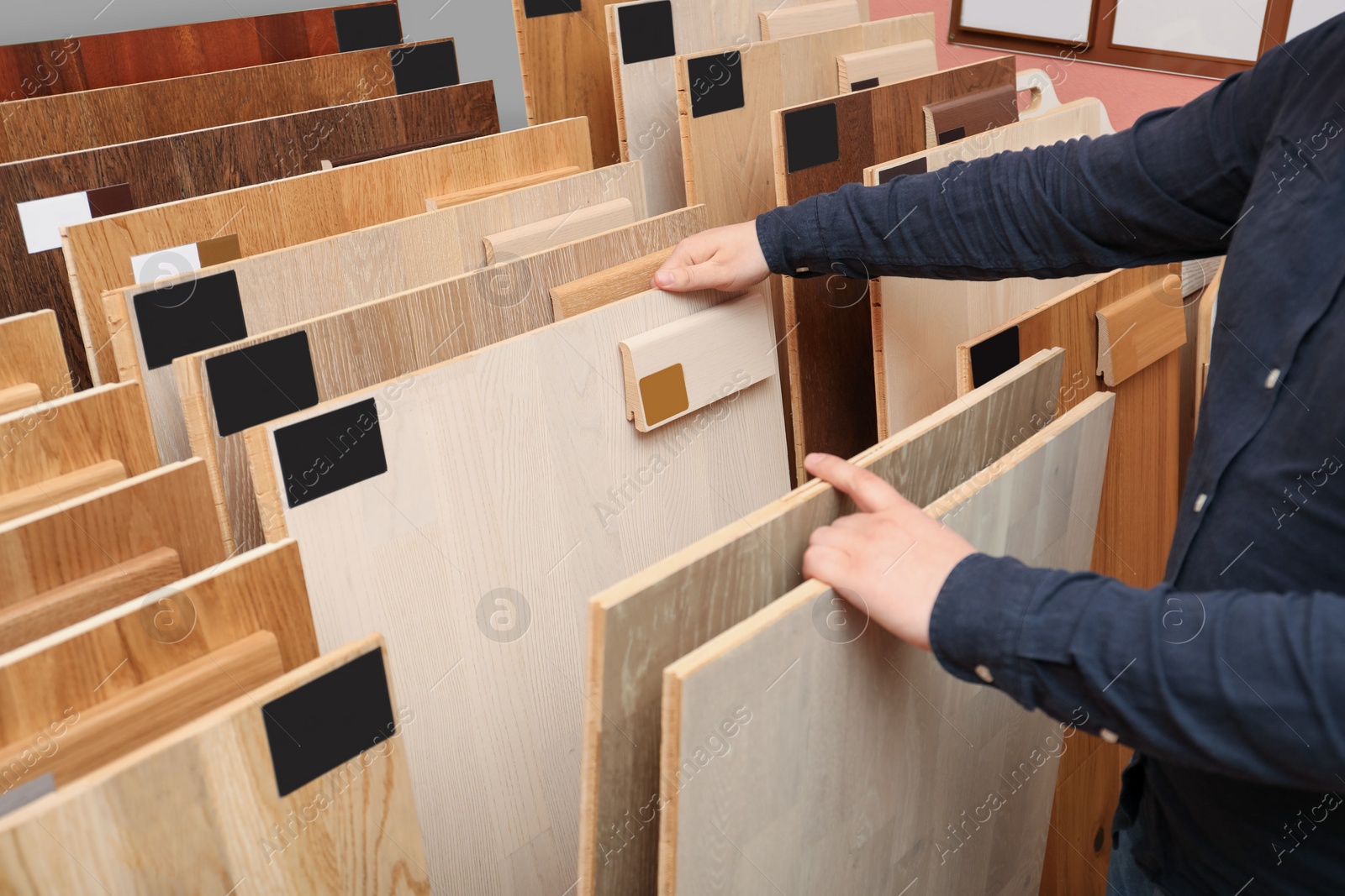 Photo of Man choosing wooden flooring among different samples in shop, closeup