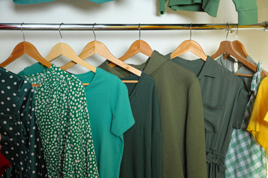 Photo of Different green clothes on wooden hangers in wardrobe. Fashion blogger