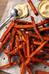 Delicious sweet potato fries and sauce on wooden table, top view