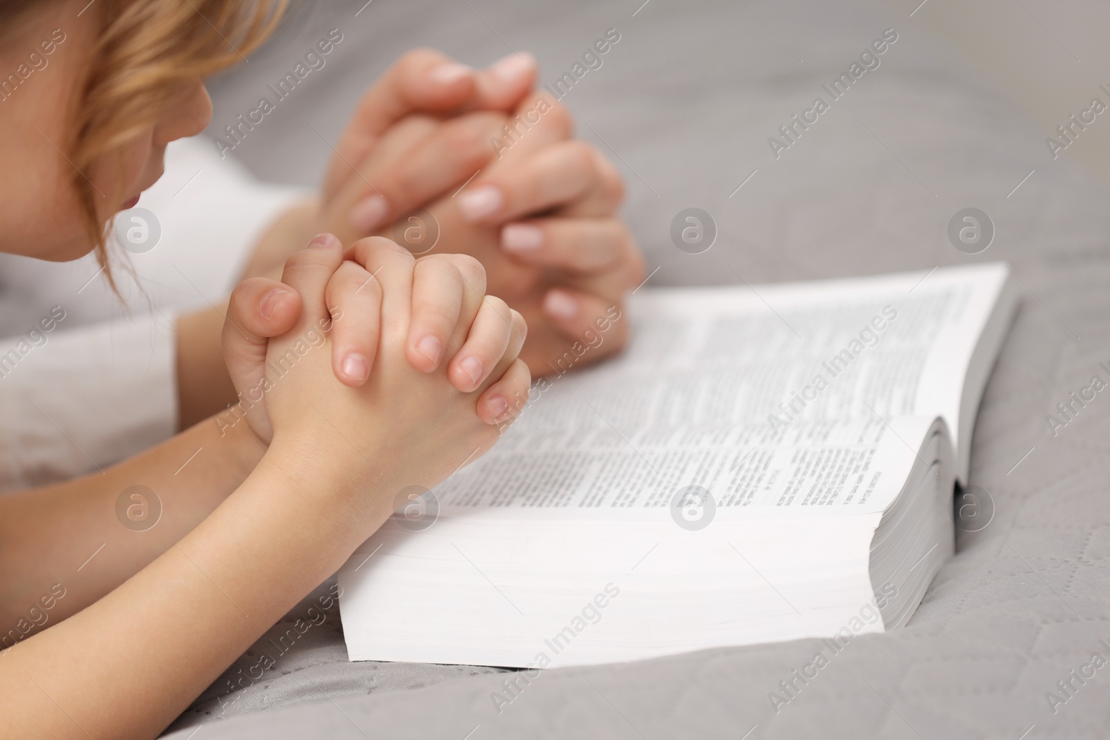 Photo of Girl and her godparent praying over Bible together indoors, closeup. Space for text