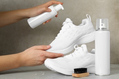 Photo of Woman cleaning stylish footwear on grey marble background, closeup. Shoe care accessories