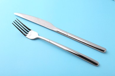 Photo of Stylish cutlery. Silver knife and fork on light blue background