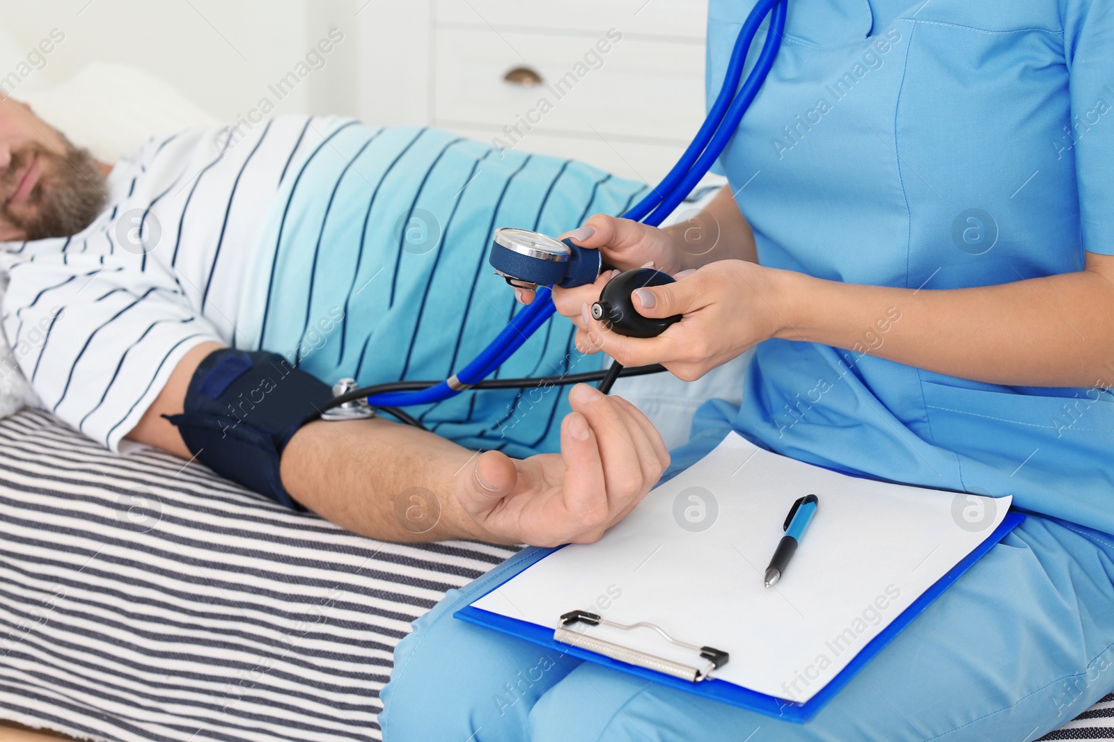 Photo of Female medical assistant measuring male patient blood pressure during home visit