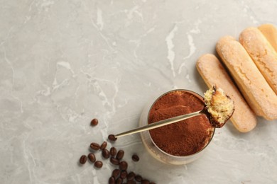 Photo of Tasty tiramisu in glass, coffee beans, spoon and biscuits on light grey table, flat lay. Space for text