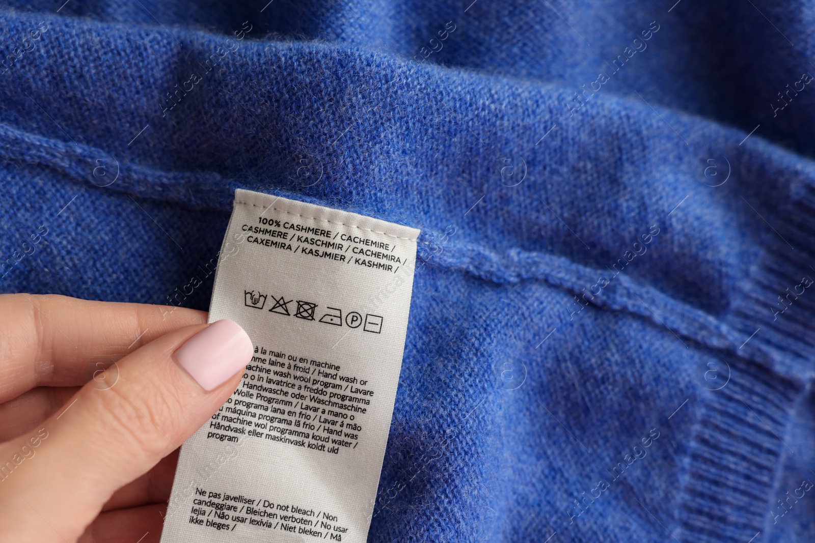 Photo of Woman holding clothing label in different languages on blue garment, closeup