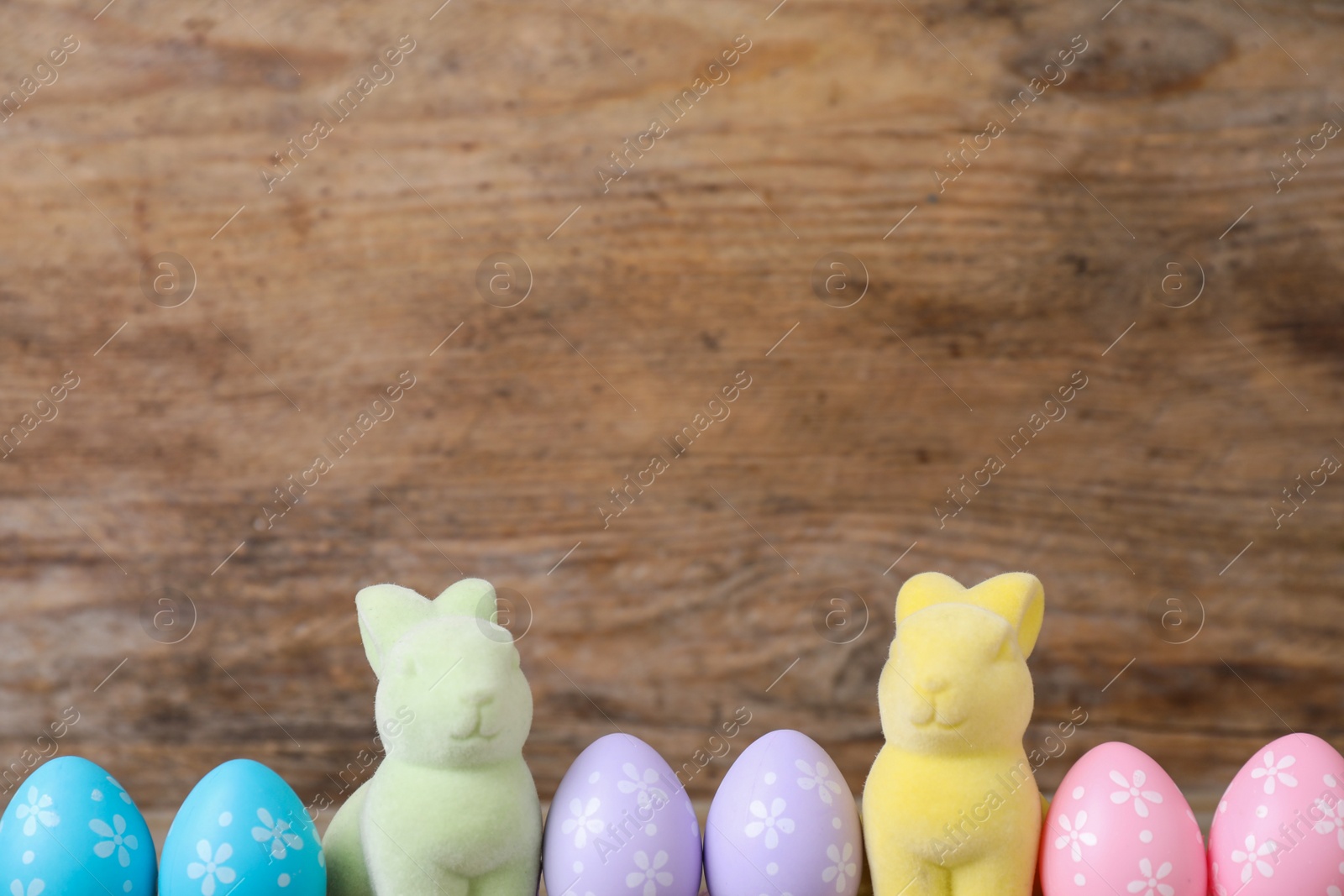 Photo of Easter bunnies and painted eggs on wooden background, space for text