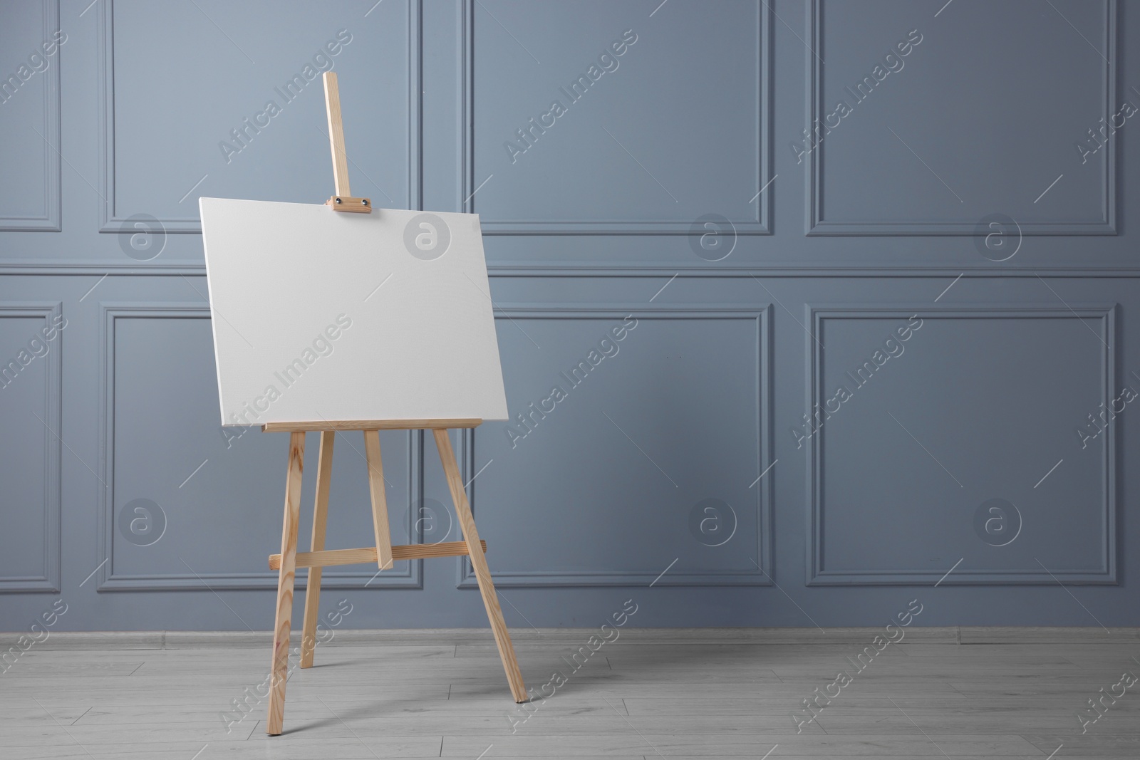 Photo of Wooden easel with blank canvas near grey wall indoors. Space for text