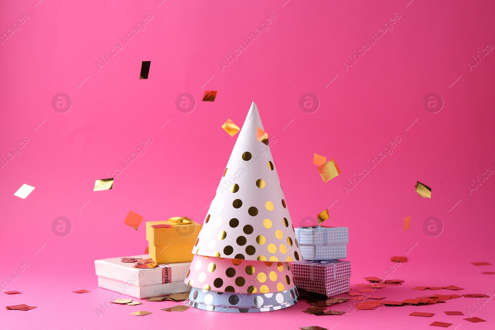 Photo of Party hats, gift boxes and confetti on pink background