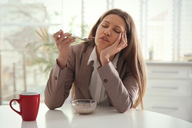 Photo of Sleepy young woman eating breakfast at home in morning