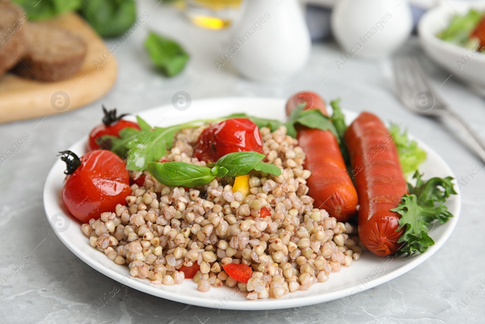 Photo of Tasty buckwheat porridge with sausages on light grey marble table