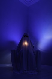 Photo of Creepy ghost. Woman covered with sheet in armchair in blue light