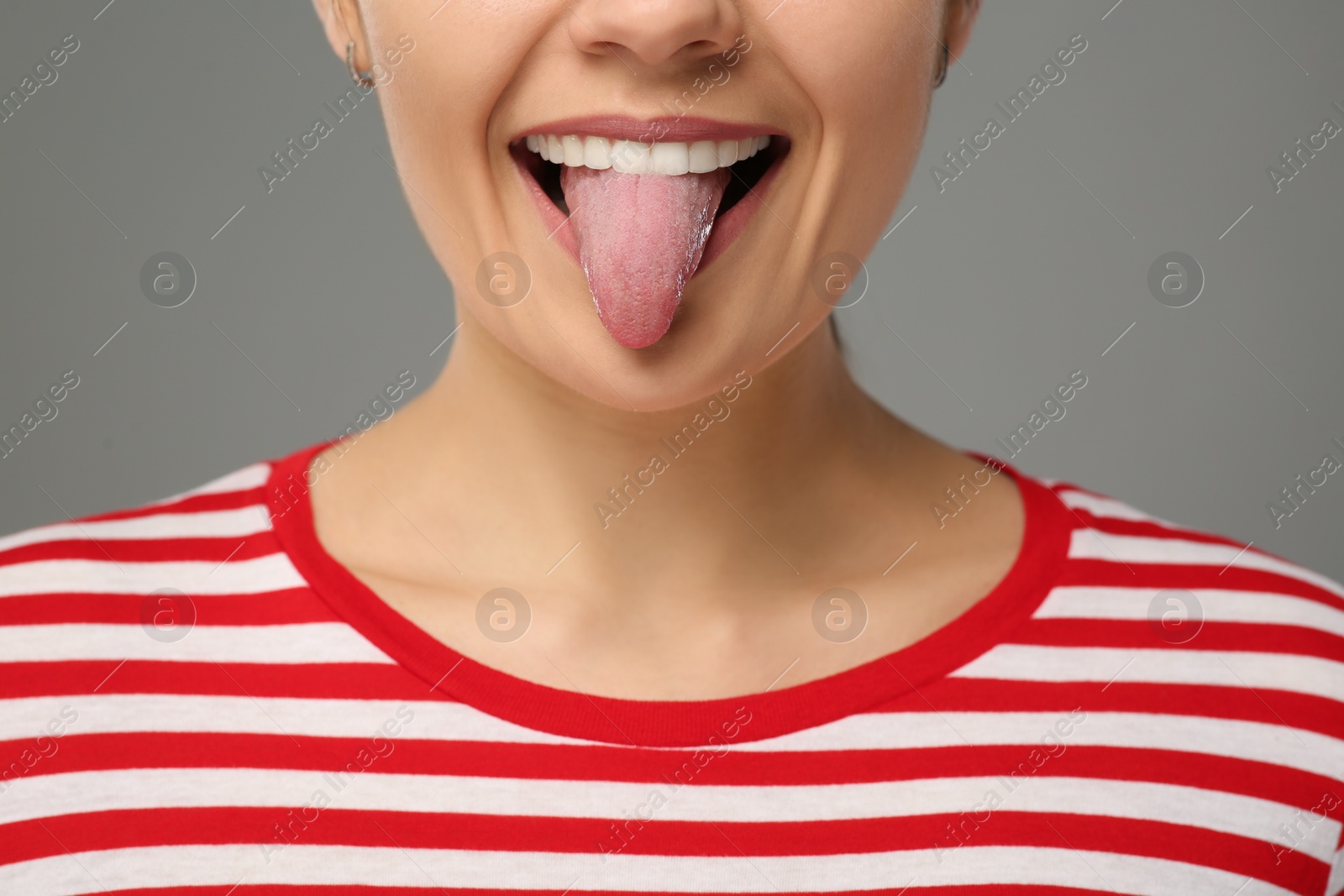 Photo of Happy young woman showing her tongue on grey background, closeup